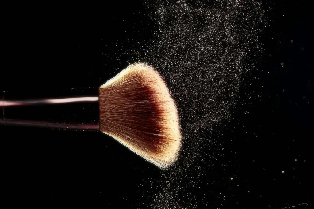 Makeup brush with a puff of powder on a black background